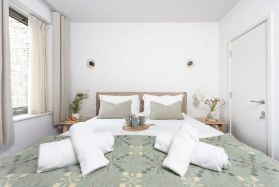 Bright bedroom with a double bed, decorative pillows, and plants on bedside tables.