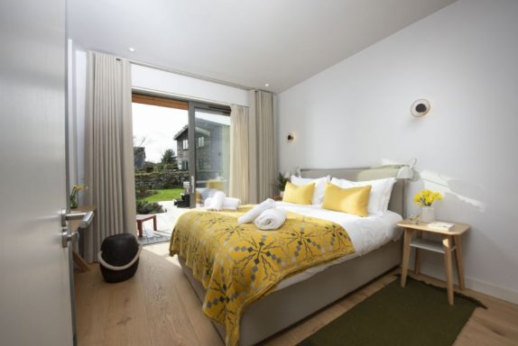 Bright bedroom with yellow accents, opening to a garden through large glass doors.