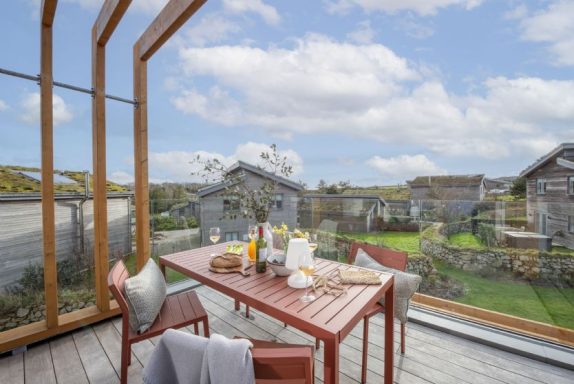 A terrace with a dining table set against a scenic rural backdrop and cloudy sky.