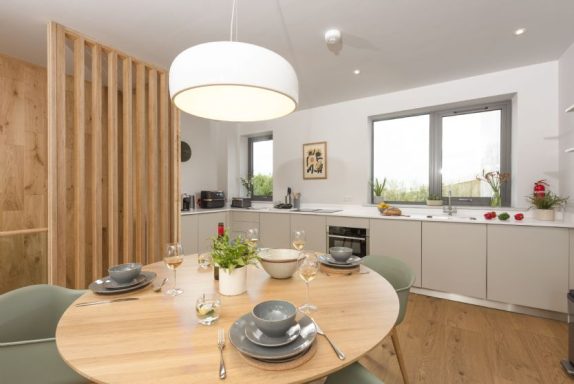 Modern kitchen and dining area with a wooden table, green chairs, and bright natural light.