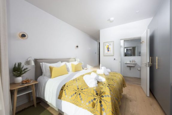 Bright, modern bedroom with a double bed, yellow accents, and an ensuite bathroom.