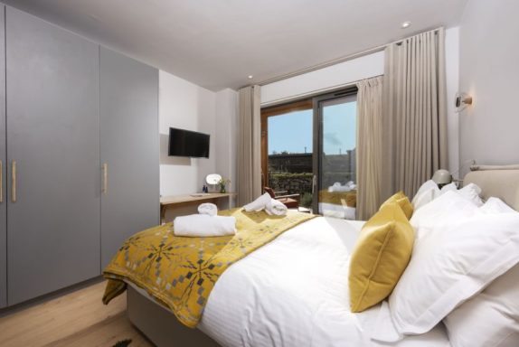 Modern bedroom featuring a large bed, yellow accents, and natural light from a window.