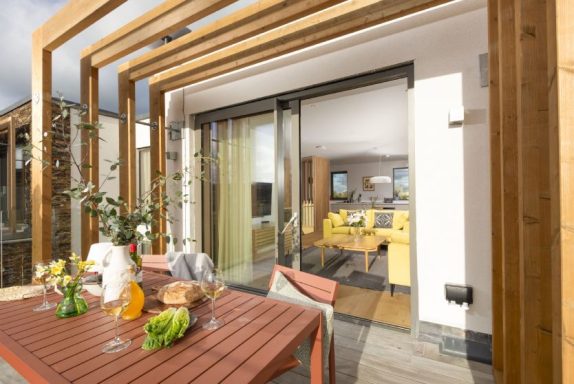 Modern balcony with wooden beams, a dining table, and a view of a bright living area.
